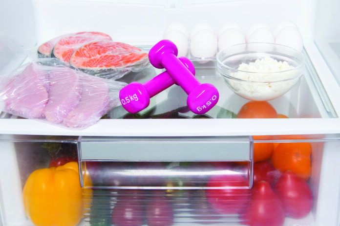 on the shelves of a white refrigerator, food supply, fresh vegetables, meat, fish, eggs, cottage cheese and pink dumbbells for sports, close-up